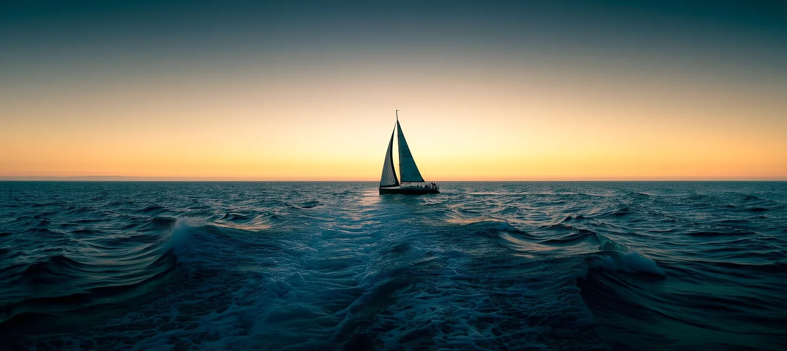 A lone sailboat under sail on the open ocean at sunset